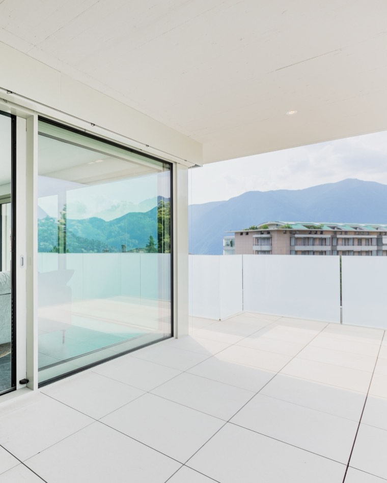 Baie vitrée coulissante et garde-corps en verre sur une terrasse avec vue sur le lac et les montagnes